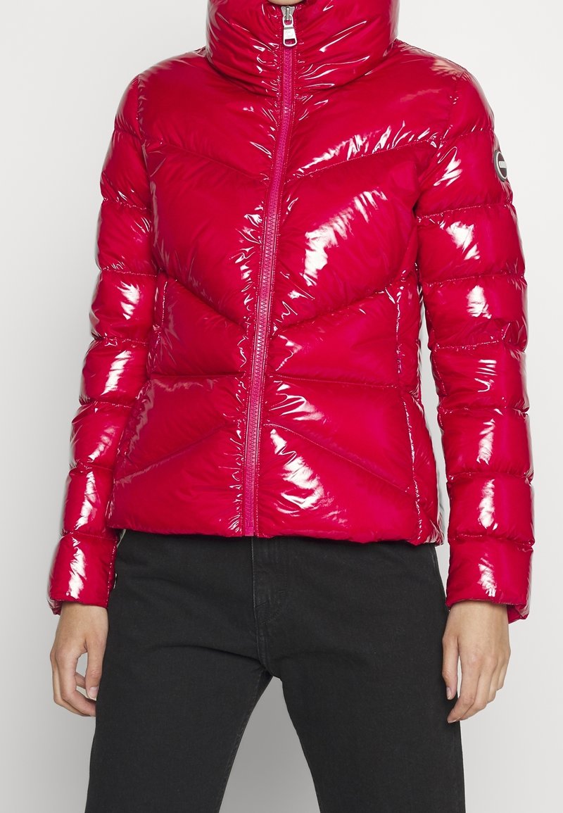 Skinande, isolerad puffjacka i starkt rosa med hög krage och blixtlås framtill. Har ett chevron-quiltmönster och elastiska muddars.