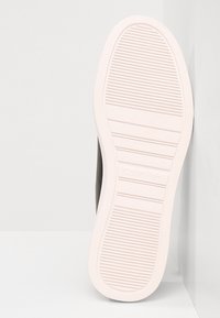 Semelle d'une basket blanche Calvin Klein avec des motifs à côtes horizontales et le nom de la marque embossé près de la zone de la voûte plantaire.