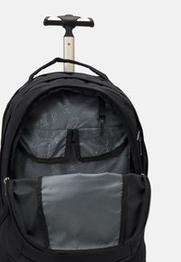 Schwarzer Rollrucksack mit einem teleskopischen Griff, ausgestattet mit einem Stoffaußenmaterial, einem geräumigen Fach und einem grauen Innenraum mit Organisationsfächern.