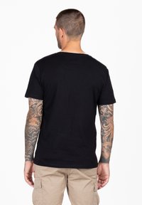 Camiseta de algodón negra con cuello redondo y mangas cortas, vista desde la parte de atrás. Presenta una textura suave y un corte regular.