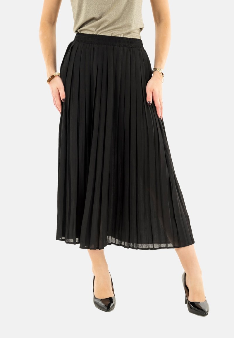 Jupe midi plissée noire avec une taille élastique, présentant un design fluide. Associée à des talons en vernis noir.