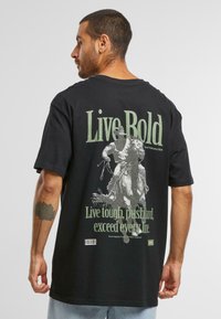 Black t-shirt featuring "Live Bold" text in green on the back, with a graphic of a rider on a horse, and smaller text below. Short sleeves.