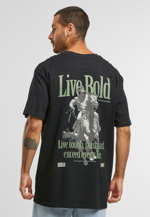 T-shirt noir avec le texte "Live Bold" en vert à l'arrière, accompagné d'un graphique d'un cavalier sur un cheval, et d'un texte plus petit en dessous. Manches courtes.
