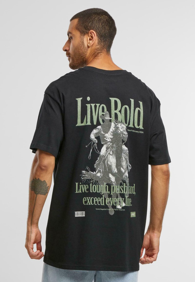 Black t-shirt featuring "Live Bold" text in green on the back, with a graphic of a rider on a horse, and smaller text below. Short sleeves.