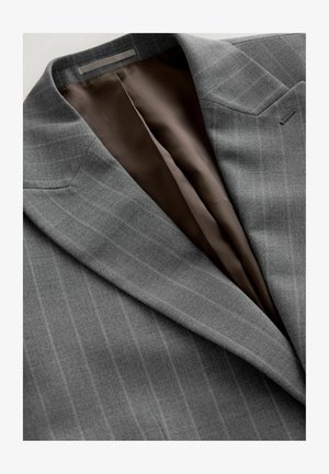 Chaqueta de traje gris con finas rayas verticales, que cuenta con un forro de satén marrón. Los detalles notables incluyen solapas afiladas y un bolsillo.