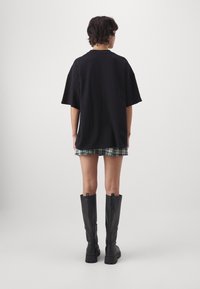 Camiseta negra de gran tamaño con hombros caídos, combinada con una falda de cuadros verde y botas negras hasta la rodilla con suelas gruesas.
