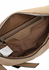 Interno di borsa beige con foderature morbida e testurizzata, tasca con zip e etichetta di cura visibile. Presenta una chiusura in zip metallica e dettagli in pelle.