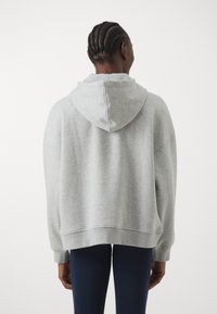 Sivá oversized mikina s kapucňou na šnúrku, ribbovanými manžetami a lemom. Má mäkkú textúru a ležérny dizajn. Nosí sa s námorníckymi legínami.