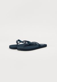 Tongs bleu marine avec des semelles texturées, des fines lanières et un logo blanc sur les côtés. Le matériau semble être en caoutchouc et flexible.