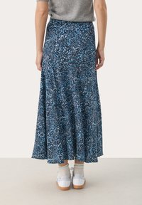 Szeroka spódnica maxi w granatowym kolorze z wielokolorowym abstrakcyjnym wzorem, wykonana z lekkiego, teksturowanego materiału, zestawiona z białymi sneakersami i skarpetkami.
