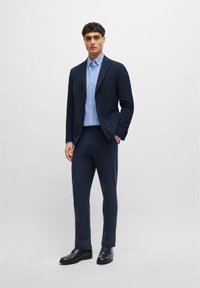 Navy suit with a tailored blazer and matching trousers, paired with a light blue button-up shirt and black leather shoes.