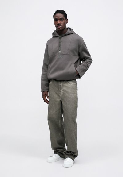 Hanorac gri cu siret și jumătate de fermoar, asortat cu blugi largi gri deschis și teniși albi. Design simplu și casual.