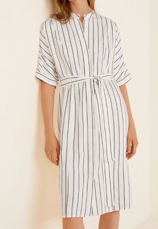 Vestido blanco de botones con rayas verticales negras, mangas cortas, cinturilla ceñida, hasta la rodilla, textura de tela suave.