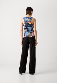 Multicolored tank top with abstract patterns, sleeveless design, smooth fabric. Paired with black wide-leg trousers and high-heeled shoes.