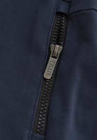 Un tissu bleu marine au toucher lisse qui comporte une fermeture éclair sur le côté gauche, une tirette en métal avec gravure, et une bande de fermeture éclair noire contrastante.