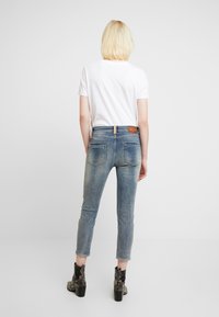 Světle modré slim-fit džíny s vybledlým vzhledem, obsahující koženou nášivku se značkou, čtyři kapsy a ohrnuté manžety. Nosí se s bílým tričkem.