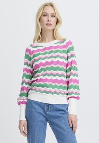 Pull multicolore présentant des rayures en zigzag rose, vert et blanc, avec des poignets et un ourlet côtelés, confectionné dans un matériau en maille douce.