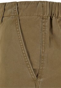 Gros plan d’un pantalon en tissu marron avec une poche avant en biais et un détail de ceinture élastique.