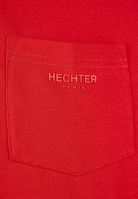 T-shirt rouge doté d'une poche arrière avec le texte embossé "HECHTER PARIS". Texture lisse avec une coupe ajustée et des détails de surpiqûres contrastantes.