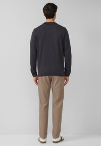 Donkergrijze gebreide trui met een gestructureerd patroon, lange mouwen en een kraag, gecombineerd met lichtbeige broek en witte sneakers.