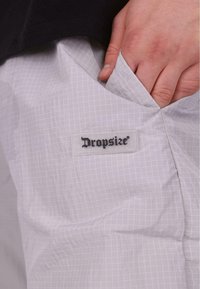 Jasnoszare spodnie wykonane z teksturowanej tkaniny w kratkę. Czerna metka "Dropsize" jest widoczna przy kieszeni.