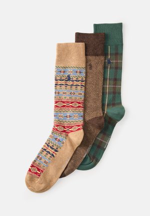 Trzy pary skarpetek: jedna z kolorowym splotem na beżowym tle, jedna brązowa w jodełkę oraz jedna zielona w kratę z akcentującą paskiem.