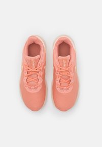 Vaaleanpunaiset urheilukengät, joissa on verkkomateriaali yläosa, nauhakiinnitys, pehmustettu nilkkaosa, tekstuuri ja huomaamattomat keltaiset yksityiskohdat.