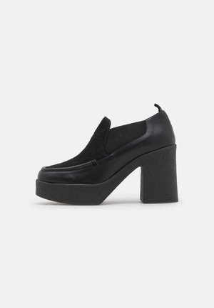 Sort platåsko med chunky høj hæl, slip-on stil og tekstureret sål, vist i sideprofil på hvid baggrund.