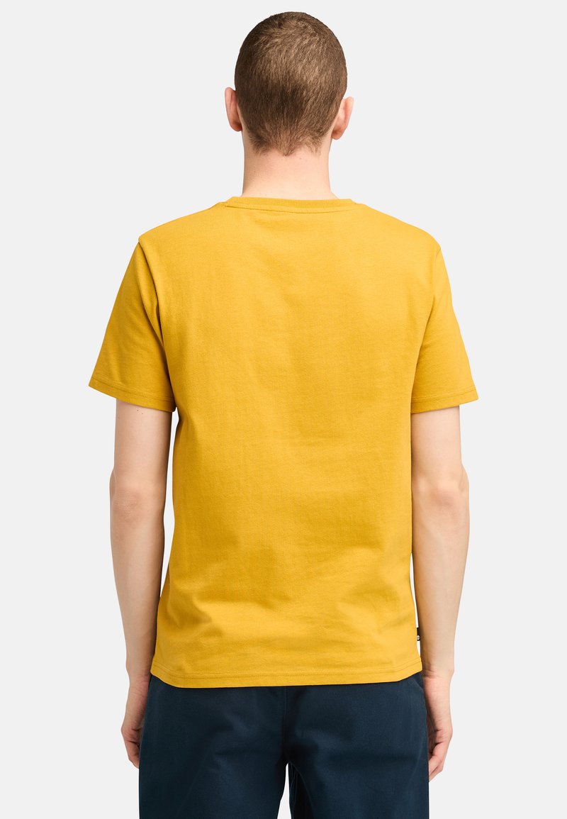 Musztardowa krótko rękawowa koszulka z okrągłym dekoltem i miękką, gładką teksturą. Eksponowana z tyłu, ukazująca proste elementy wzornictwa.