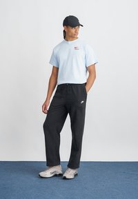 T-shirt azul claro de mangas curtas da Nike, calças pretas até os tornozelos e sapatilhas desportivas cinzentas. Apresenta um logótipo vermelho da Nike na t-shirt e nas calças.