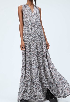 Femme portant une robe longue sans manches à motif avec une jupe fluide et des bottines noires épaisses à lacets.
