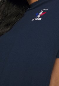 Camiseta de manga corta en color navy, hecha de algodón, con el logo bordado de Adidas en el pecho en tonos rojo, blanco y azul.