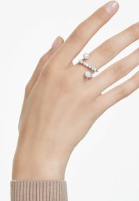 Drei Ringe an einer Hand: einer mit einer Perle, ein weiterer mit kleinen klaren Edelsteinen und einem größeren Stein in der Mitte; aus Silber; minimalistisches Design.