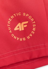 Tissu rouge avec un logo jaune "4F" centré dans un cercle de texte indiquant "AUTHENTIC SPORTSWEAR BRAND" et des coutures blanches le long de l'ourlet.