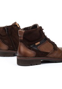 Stivali ankle in pelle marrone e suede con chiusura a zip, lacci, texture a contrasto, suola marrone e dettagli di cucitura delicati.