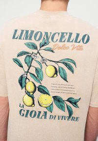 Бежова риза с отпечатано клонче с лимон, лимони и текст "Limoncello Dolce Vita La Gioia di Vivere" на гърба.