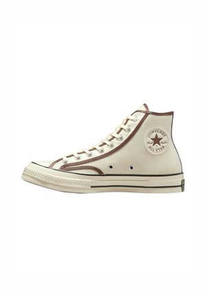 Zapatillas altas de lona color crema con acentos marrones, que cuentan con un parche de logo redondo, ojales de metal y una suela de goma.