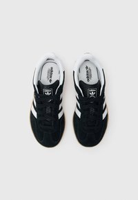 Črni semiš supergi z belimi črtami in gumijastim podplatom. Klasičen vezalni dizajn z oblazinjenim ovratnikom in logotipom na jezičku.