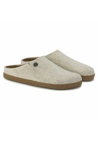 Wool clogs with a soft beige exterior and a curved design. Features a tan rubber sole and a small metal logo accent on the side.