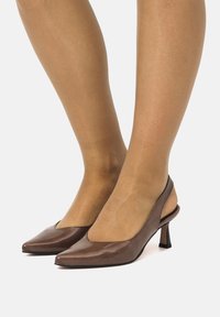 Tacchi slingback marroni con punta affusolata, caratterizzati da una finitura lucida e un tacco a blocco sottile. Texture liscia e design minimalista.