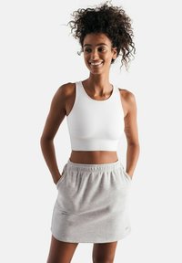 Top corto bianco a coste con spalline larghe abbinato a una gonna elastica grigia chiara con tasche laterali e una texture morbida.