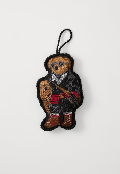 Vezeni filcani privjesak u obliku medvjeda koji nosi sunčane naočale, crni kaput s crvenim akcentima i smeđe čizme. Uključuje petlju za kačenje.