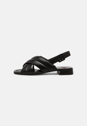Black leather sandals with a crisscrossed design, adjustable buckle strap, and a flat sole. Features a sleek, minimalistic shape.