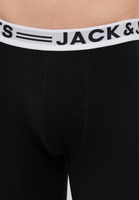Schwarze Baumwoll-Boxershorts mit einem weißen elastischen Bund, auf dem "JACK & JONES" in Schwarz gedruckt ist. Glatte Textur und enganliegendes Design.