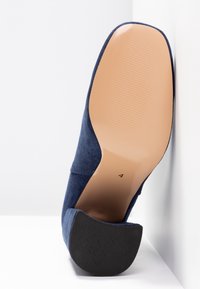 Talons en daim bleu marine avec une silhouette arrondie, une texture lisse et mate, et une semelle en caoutchouc marron contrastante dotée d'un motif d'adhérence texturé.