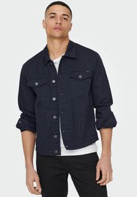 Giubbotto in denim navy con collo a camicia, maniche lunghe arrotolate fino ai gomiti, due tasche frontali e dettagli in bottone argentato.