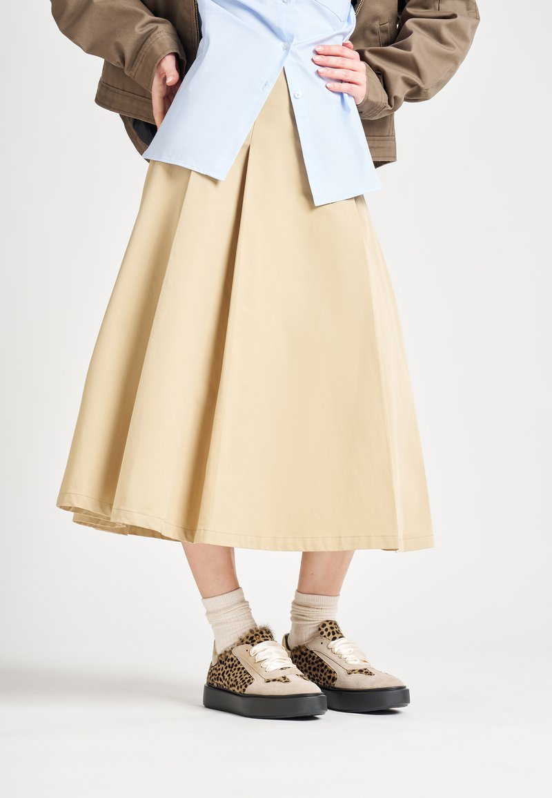 Gonna a trapezio beige realizzata in tessuto morbido, indossata con una camicia azzurro chiaro e sneakers con stampa leopardata. Presenta calze a coste color crema.