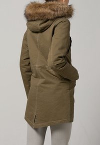 Khaki parka med en foderad huva, med märkbara sömdetaljer och raka linjer, designad för värme och stil.