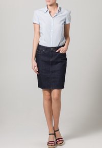 Falda de lápiz de mezclilla en azul oscuro, combinada con una blusa de cuadros de gingham en azul claro. Las sandalias presentan un diseño de tiras multicolores.