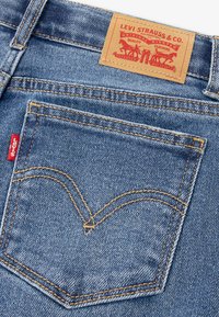 Levi's plave traperice s posebnim stražnjim džepom koji ima žute šavove i prepoznatljivi V-oblik dizajn. Etiketa glasi "Levi Strauss & Co."
